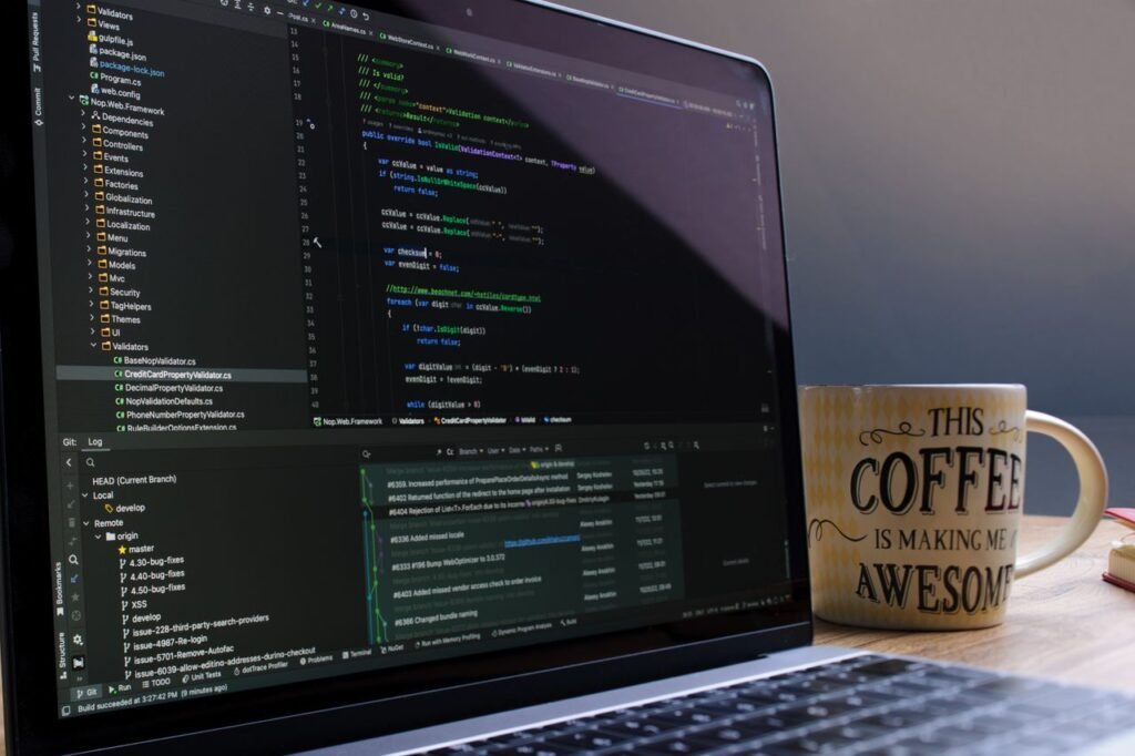 Close-up of laptop with coding software and a motivational coffee mug on a desk.